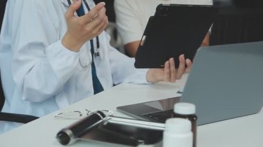 Doktorun tablet bilgisayarda çalışması ve modern hastane masasında tıbbi raporları tartışması..