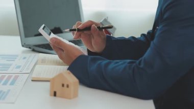 İş adamı hesap makinesi üzerinde çalışıyor. Ofiste ev modeli olan bir laptop..