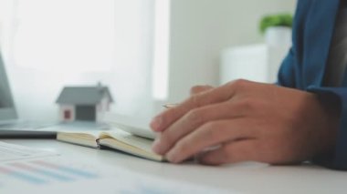 İş adamı hesap makinesi üzerinde çalışıyor. Ofiste ev modeli olan bir laptop..