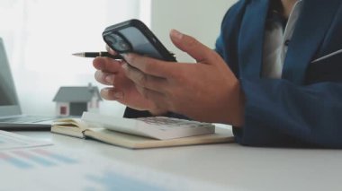 İş adamı hesap makinesi üzerinde çalışıyor. Ofiste ev modeli olan bir laptop..