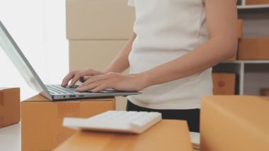 İş kadını kutular ve hesap makinesinin etrafında dizüstü bilgisayarla çalışıyor.