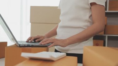 İş kadını kutular ve hesap makinesinin etrafında dizüstü bilgisayarla çalışıyor.