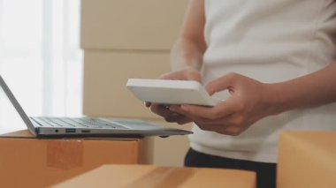 İş kadını kutular ve hesap makinesinin etrafında dizüstü bilgisayarla çalışıyor.