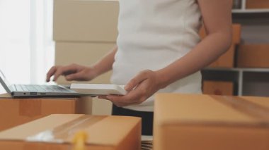 İş kadını kutular ve hesap makinesinin etrafında dizüstü bilgisayarla çalışıyor.