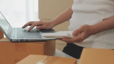 İş kadını kutular ve hesap makinesinin etrafında dizüstü bilgisayarla çalışıyor.