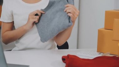 Küçük bir girişimci ya da serbest çalışan bir Asyalı kadın bir dizüstü bilgisayarda ambalaj kutularıyla çalışıyor.