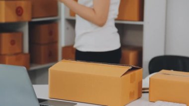 Küçük bir girişimci ya da serbest çalışan bir Asyalı kadın bir dizüstü bilgisayarda ambalaj kutularıyla çalışıyor.