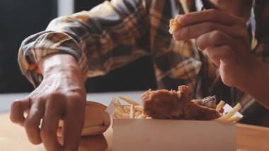 Tavuklu hamburger ve patates kızartması yiyen kişi.  