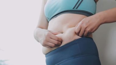 Genç bir kadın, kilolu olmanın zorluklarını simgeleyen göbeğine dokunur..