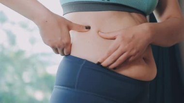 Genç bir kadın, kilolu olmanın zorluklarını simgeleyen göbeğine dokunur..