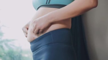 Genç bir kadın, kilolu olmanın zorluklarını simgeleyen göbeğine dokunur..