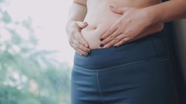 Genç bir kadın, kilolu olmanın zorluklarını simgeleyen göbeğine dokunur..