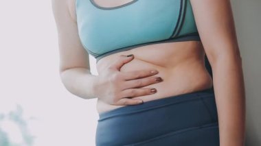 Genç bir kadın, kilolu olmanın zorluklarını simgeleyen göbeğine dokunur..