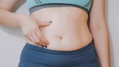 Genç bir kadın, kilolu olmanın zorluklarını simgeleyen göbeğine dokunur..