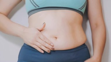 Genç bir kadın, kilolu olmanın zorluklarını simgeleyen göbeğine dokunur..