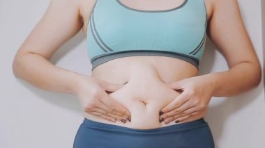 Genç bir kadın, kilolu olmanın zorluklarını simgeleyen göbeğine dokunur..