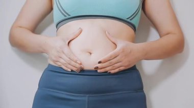 Genç bir kadın, kilolu olmanın zorluklarını simgeleyen göbeğine dokunur..