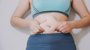 Genç bir kadın, kilolu olmanın zorluklarını simgeleyen göbeğine dokunur..