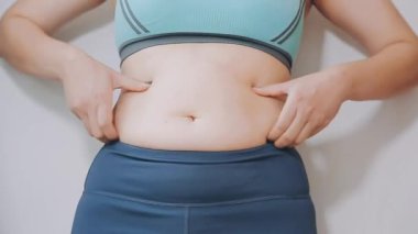 Genç bir kadın, kilolu olmanın zorluklarını simgeleyen göbeğine dokunur..