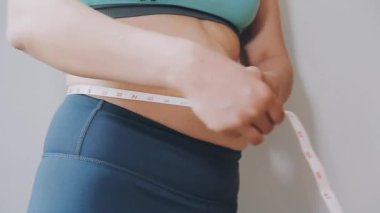 Bel ölçüsünü bantla alan genç bir kadın, kilolu olma kavramını gözler önüne seriyor..