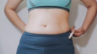 Bel ölçüsünü bantla alan genç bir kadın, kilolu olma kavramını gözler önüne seriyor..