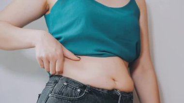 Genç bir kadın şişman karnına elleriyle dokunuyor, kilolu olma kavramını temsil ediyor.