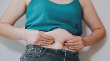 Genç bir kadın şişman karnına elleriyle dokunuyor, kilolu olma kavramını temsil ediyor.