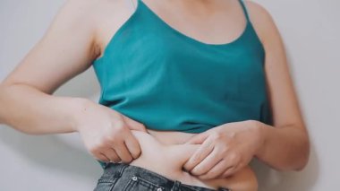 Genç bir kadın şişman karnına elleriyle dokunuyor, kilolu olma kavramını temsil ediyor.