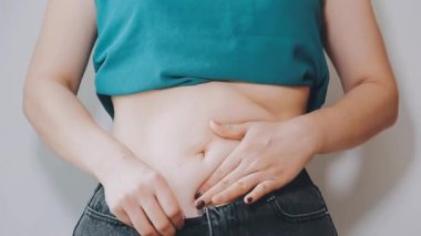 Genç bir kadın şişman karnına elleriyle dokunuyor, kilolu olma kavramını temsil ediyor.