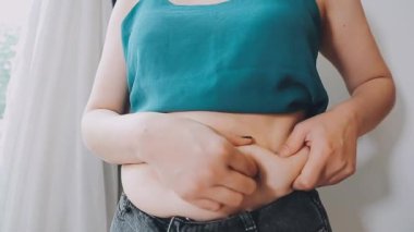 Genç bir kadın şişman karnına elleriyle dokunuyor, kilolu olma kavramını temsil ediyor.