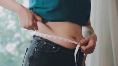 Daktilo yazan kadının kilolu konsepti ve kilo verme konsepti ölçü bandıyla belini ölçer.
