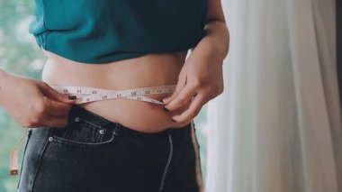 Daktilo yazan kadının kilolu konsepti ve kilo verme konsepti ölçü bandıyla belini ölçer.