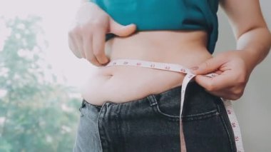 Daktilo yazan kadının kilolu konsepti ve kilo verme konsepti ölçü bandıyla belini ölçer.