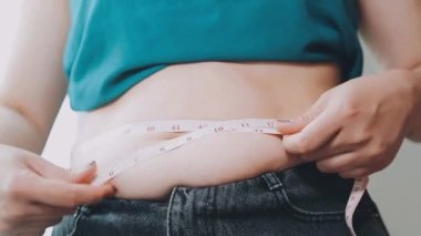 Kot pantolon giyen ve ölçü bandıyla bel ölçen genç bir kadın.