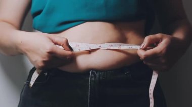 Kot pantolon giyen ve ölçü bandıyla bel ölçen genç bir kadın.