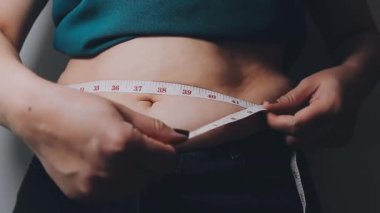 Kot pantolon giyen ve ölçü bandıyla bel ölçen genç bir kadın.