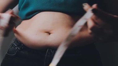 Kot pantolon giyen ve ölçü bandıyla bel ölçen genç bir kadın.