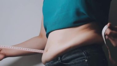 Daktilo yazan kadının kilolu konsepti ve kilo verme konsepti ölçü bandıyla belini ölçer.