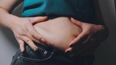 Genç bir kadının şişman karnına elleriyle dokunan kilolu bir konsept.