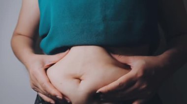Genç bir kadının şişman karnına elleriyle dokunan kilolu bir konsept.
