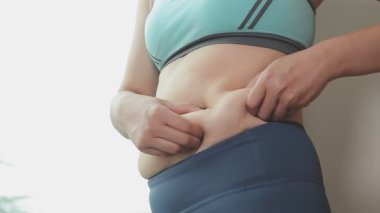 Spor giyimli genç bir kadının yakın plan görüntüsü göbeğine, kilosuna ve kilo verme konseptine dokunuyor.