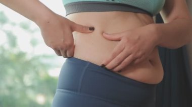Spor giyimli genç bir kadının yakın plan görüntüsü göbeğine, kilosuna ve kilo verme konseptine dokunuyor.
