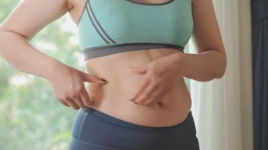 Spor giyimli genç bir kadının yakın plan görüntüsü göbeğine, kilosuna ve kilo verme konseptine dokunuyor.