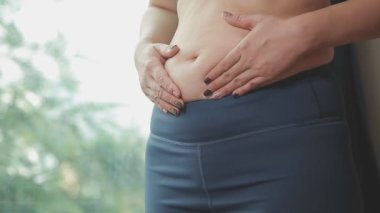 Spor giyimli genç bir kadının yakın plan görüntüsü göbeğine, kilosuna ve kilo verme konseptine dokunuyor.