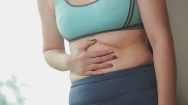 Spor giyimli genç bir kadının yakın plan görüntüsü göbeğine, kilosuna ve kilo verme konseptine dokunuyor.