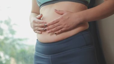 Spor giyimli genç bir kadının yakın plan görüntüsü göbeğine, kilosuna ve kilo verme konseptine dokunuyor.