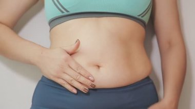 Spor giyimli genç bir kadının yakın plan görüntüsü göbeğine, kilosuna ve kilo verme konseptine dokunuyor.