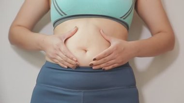 Spor giyimli genç bir kadının yakın plan görüntüsü göbeğine, kilosuna ve kilo verme konseptine dokunuyor.