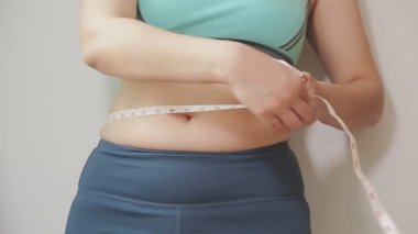 Daktilo yazan kadının kilolu konsepti ve kilo verme konsepti ölçü bandıyla belini ölçer.