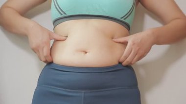 Genç bir kadının şişman karnına elleriyle dokunan kilolu bir konsept.